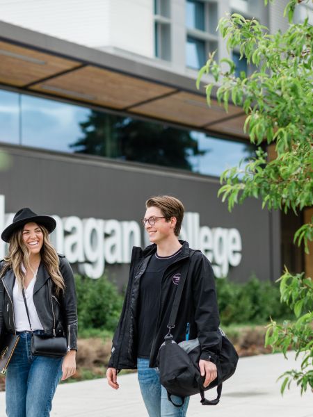 One female and one male business student walking outside in front of the  sign.